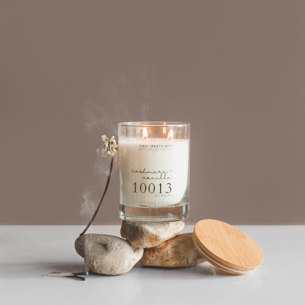 Candle labeled 'cashmere vanilla 10013' on stones with a plain background
